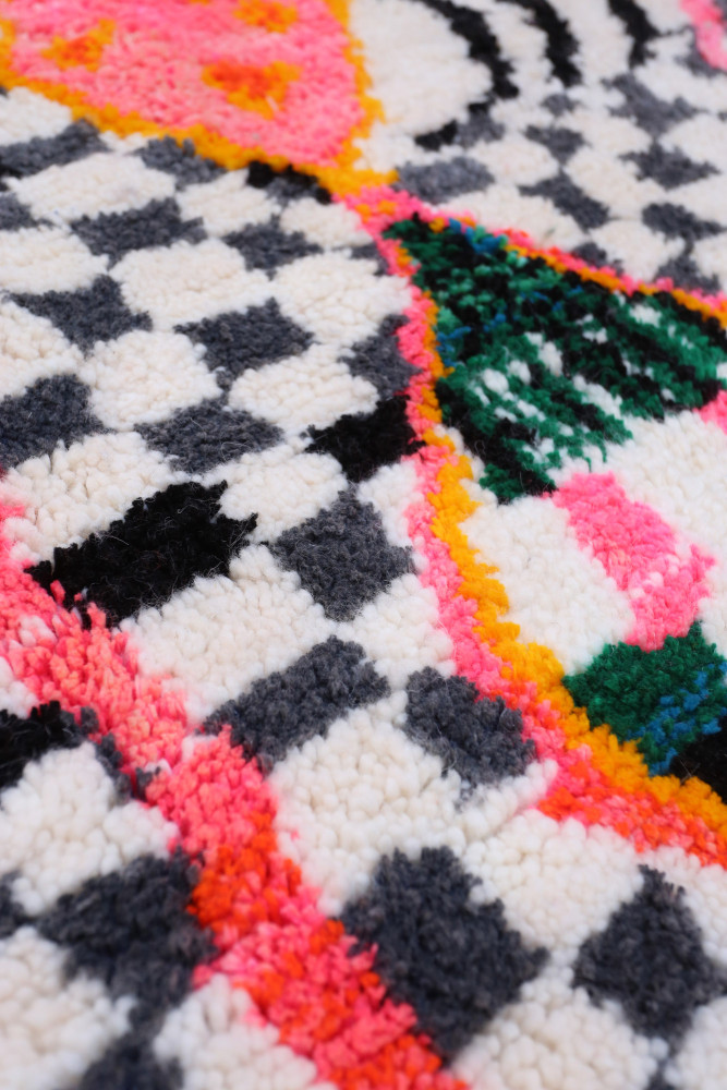 Tapis berbère aux motifs géométriques, couleurs vives comme le rose, le noir et le vert, sur fond crème.