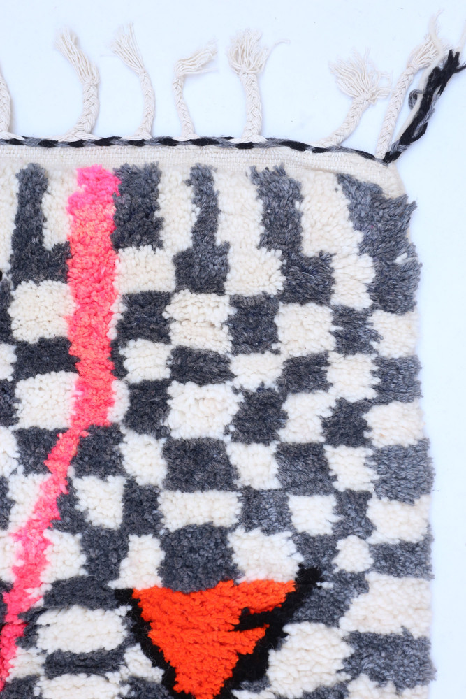 Tapis berbère au design géométrique en noir et blanc avec des motifs colorés en rose et orange.