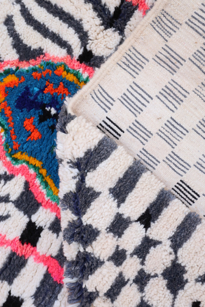 Tapis berbère coloré avec un motif géométrique en noir, blanc et des touches vives de bleu et rose.