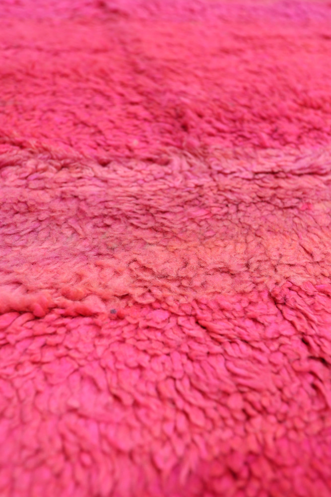 Tapis berbère en laine aux teintes roses vives avec un motif texturé et doux, parfait pour une ambiance chaleureuse.