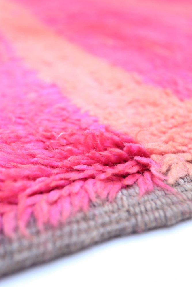 Tapis berbère aux couleurs vives de rose et orange, avec des motifs doux et texturés.