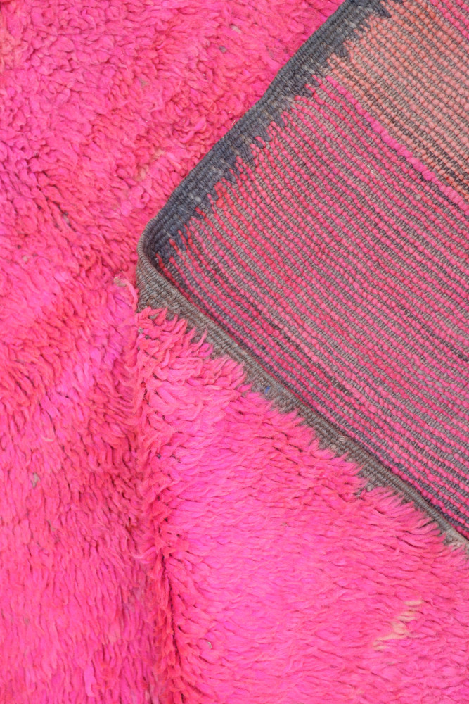 Tapis berbère coloré en rose vif avec motifs géométriques et bordure en gris, ajoutant une touche contemporaine.
