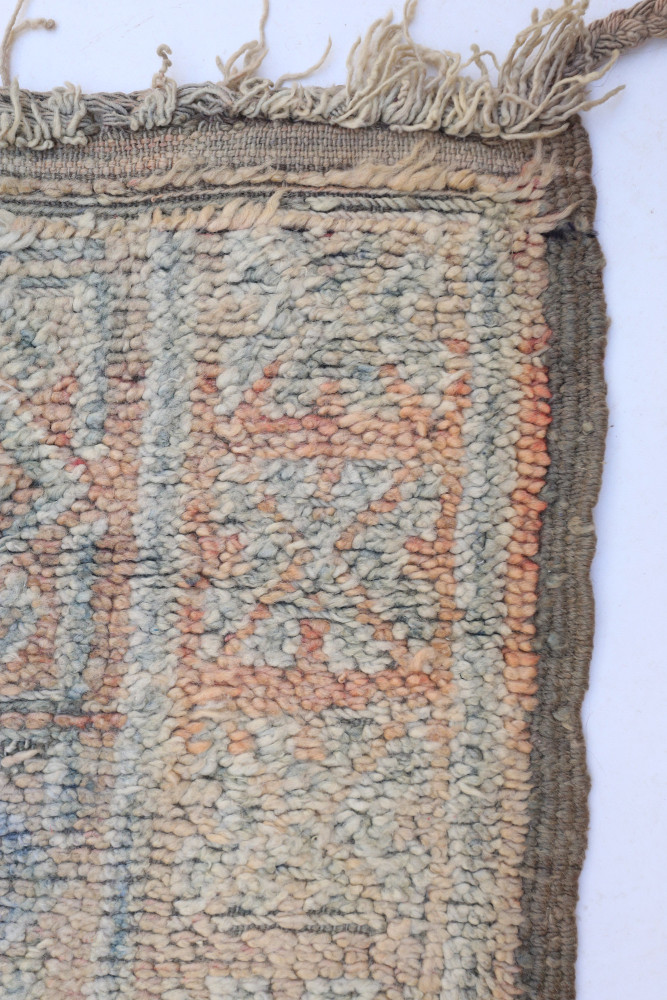 Tapis berbère aux motifs géométriques en tons bleu pâle, beige et rouille, offrant une texture riche et artisanale.
