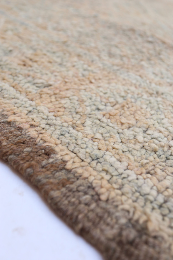 Tapis berbère en laine aux teintes neutres, présentant des motifs géométriques subtils et une texture douce.