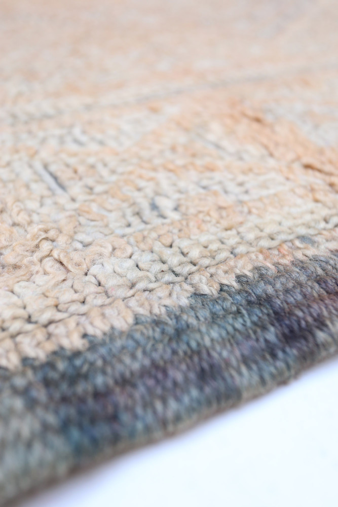 Tapis berbère aux teintes chaleureuses de beige et bleu, avec des motifs géométriques subtils et une texture douce.