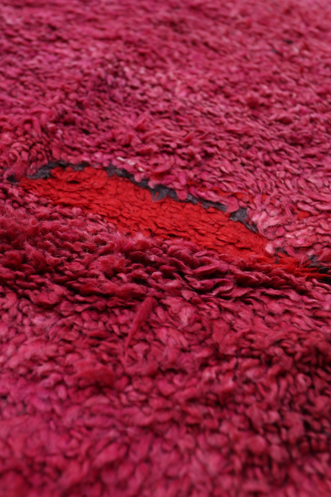 Tapis berbère en laine, avec des teintes roses et rouges, présentant une texture dense et un motif au effet shaggy.