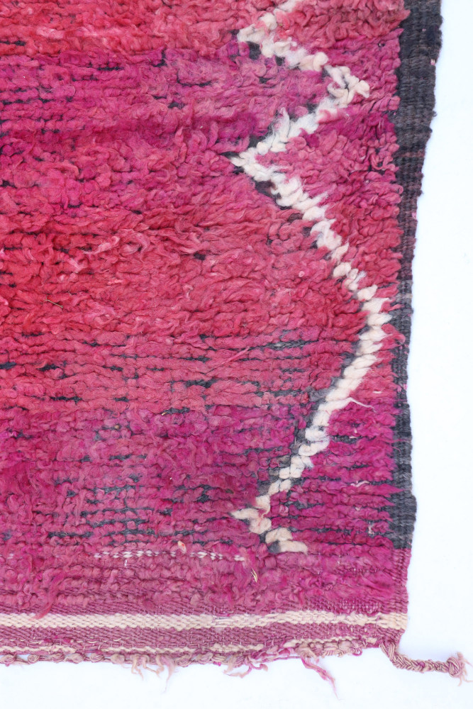 Tapis berbère aux teintes roses et rouges, orné de motifs géométriques en noir et blanc.