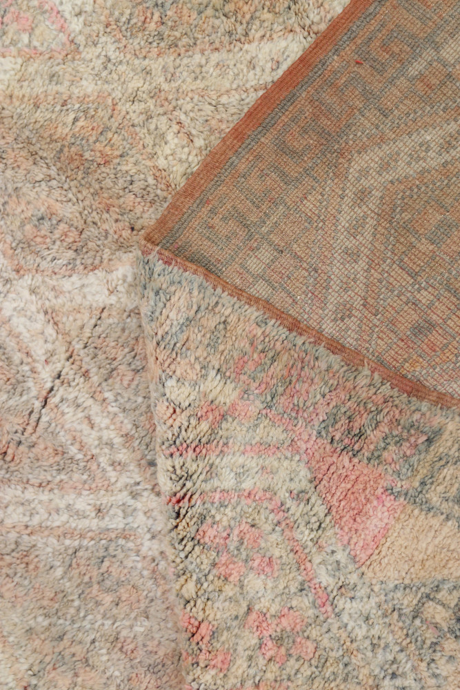 Tapis berbère en laine, avec des motifs géométriques en nuances de rose, beige et bleu, apportant chaleur et style.