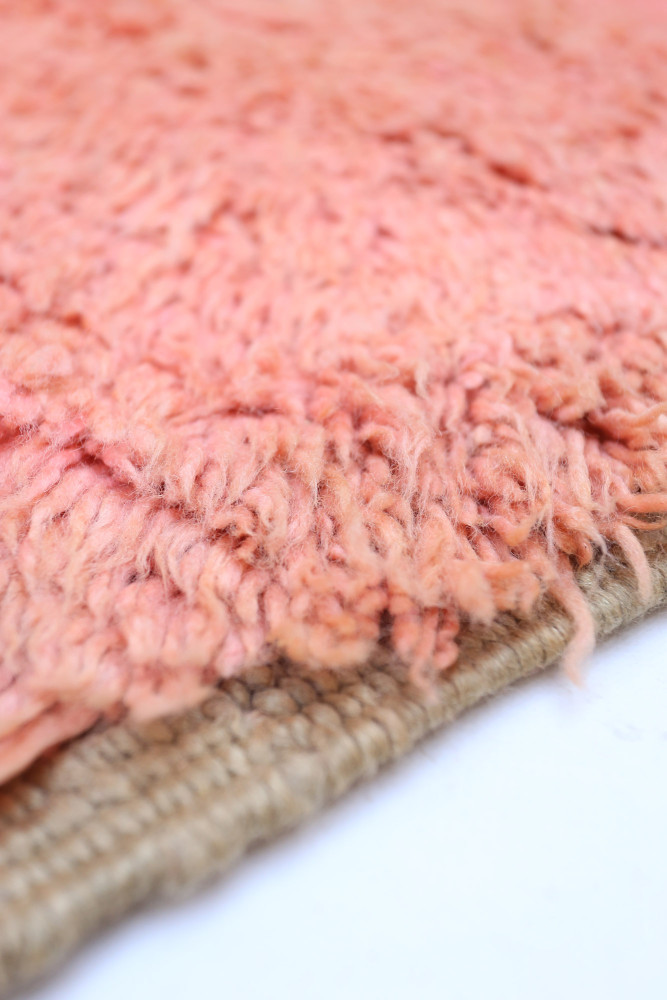 Tapis berbère en laine rose avec un motif texturé et une finition en jute, ajoutant une touche artisanale et chaleureuse.