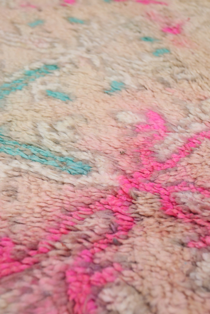 Tapis berbère aux motifs géométriques colorés, mêlant des teintes de rose, bleu et beige sur un fond doux.