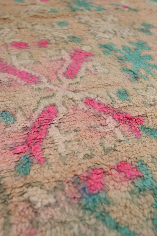 Tapis berbère aux teintes pastel avec des motifs géométriques en rose, bleu et beige, ajoutant une touche artisanale.