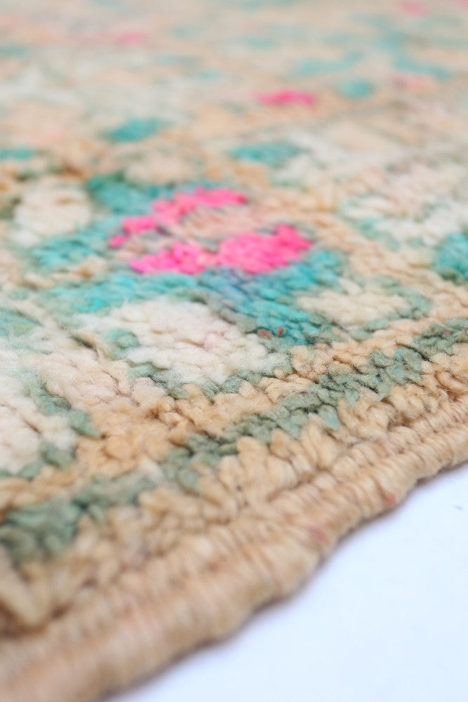 Tapis berbère aux teintes beige et vert, avec des motifs floraux en rose et turquoise sur un fond doux.