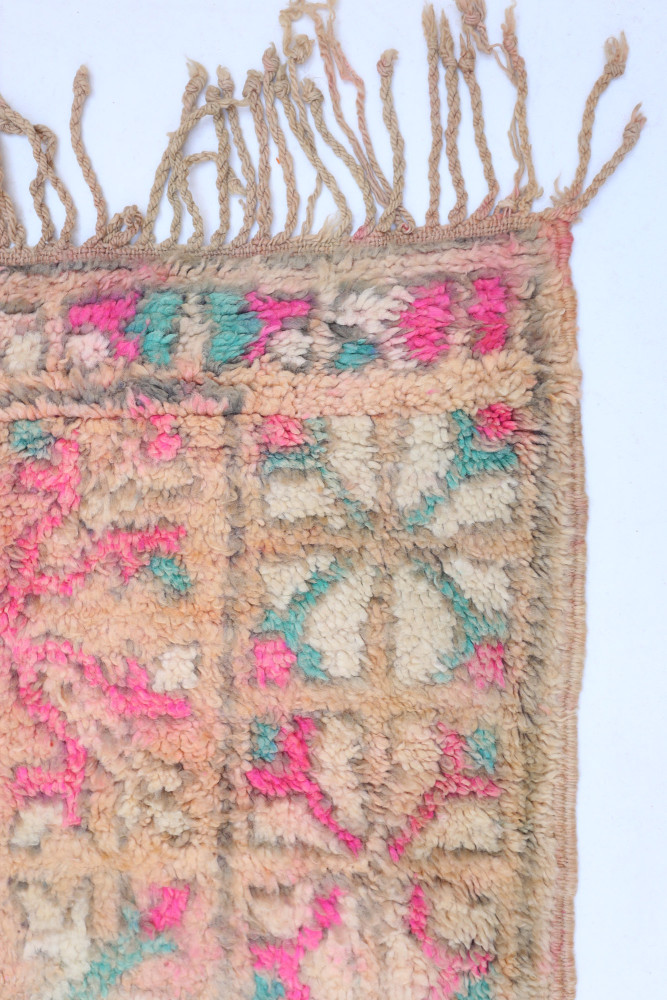 Tapis berbère en laine, aux motifs géométriques colorés de rose, beige et turquoise, ajoutant une touche artisanale.