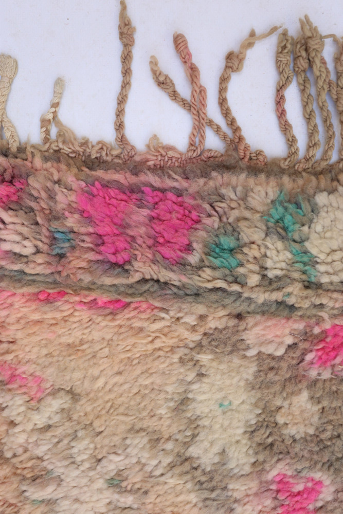 Tapis berbère aux motifs colorés, dominé par des nuances de rose, vert et beige, avec des franges délicates.