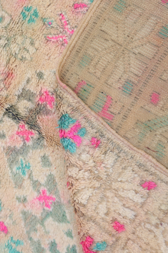 Tapis berbère aux motifs colorés, dominé par des tons beiges, roses et bleus avec des motifs géométriques distincts.