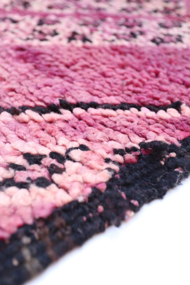 Tapis berbère aux nuances de rose, noir et motifs traditionnels géométriques.