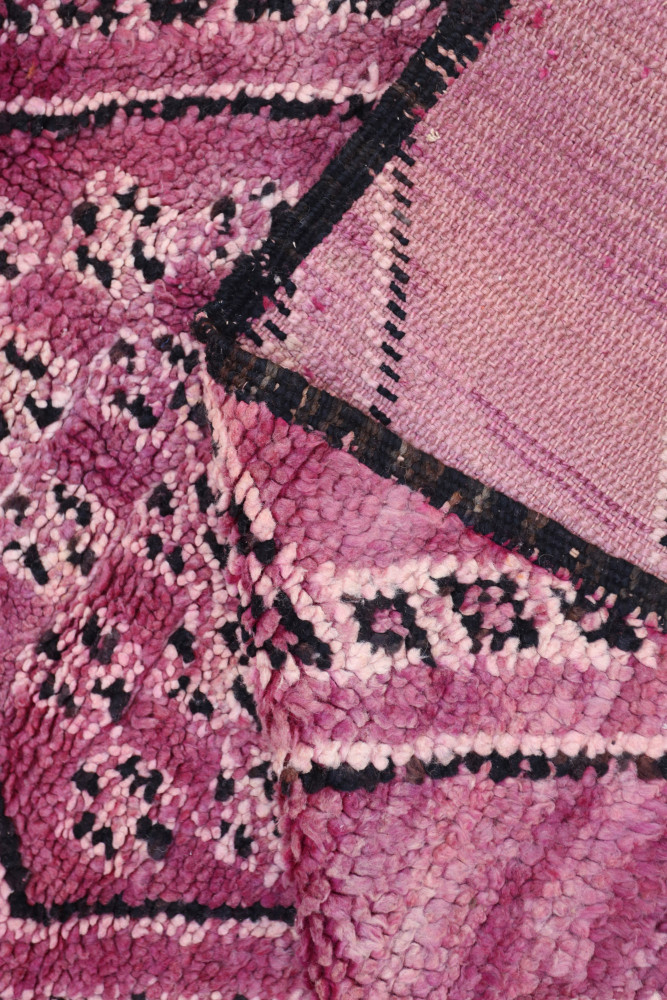 Tapis berbère aux nuances de rose avec motifs géométriques noirs sur fond texturé.