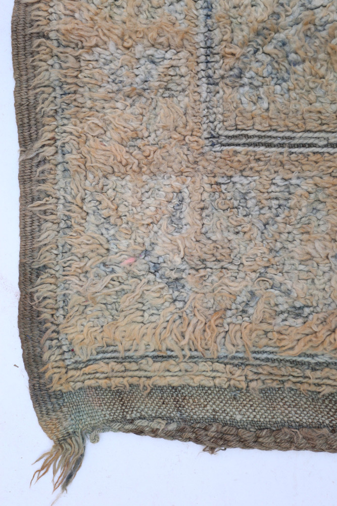 Tapis berbère aux motifs géométriques en tons de beige et bleu, avec une texture douce et un design artisanal unique.