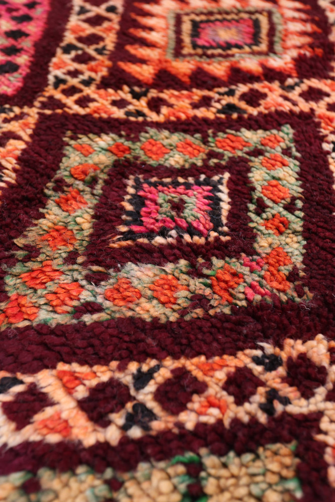 Tapis berbère aux motifs géométriques colorés dans des tons riches de rouge, orange et vert.