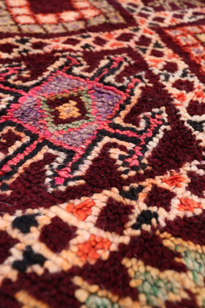 Tapis berbère riche en couleurs terre, motifs géométriques et nuances de rouge, rose et beige.