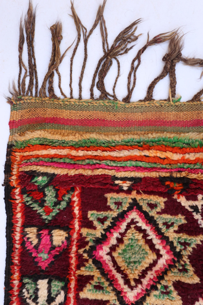Tapis berbère coloré avec des motifs géométriques en rouge, vert, rose et orange, reflets de traditions artisanales.
