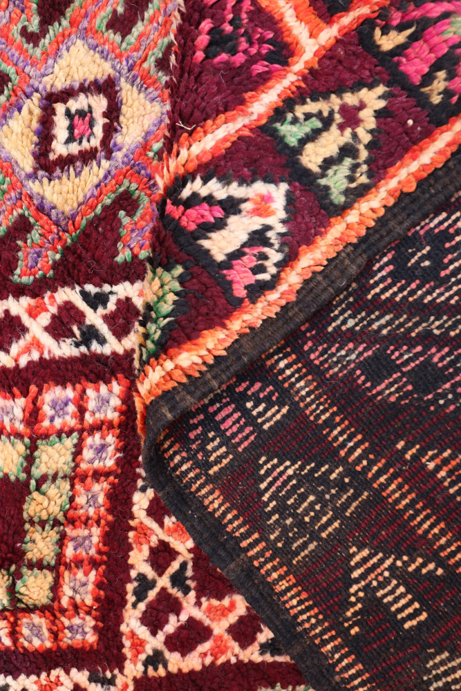 Tapis berbère coloré avec des motifs géométriques en rouge, noir, vert et beige, apportant une touche artisanale chaleureuse.