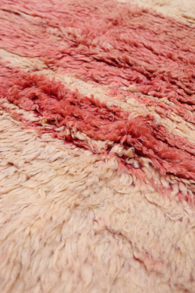 Tapis berbère en laine naturelle avec des nuances de rose, beige et des motifs texturés authentiques.