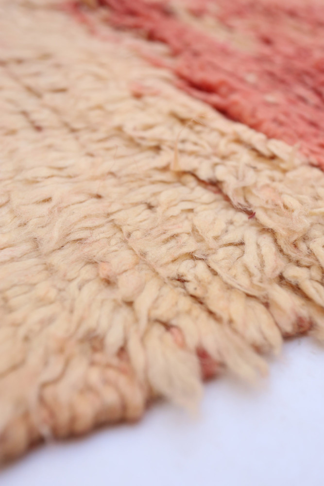 Tapis berbère en laine aux couleurs beige et rouge avec un style texturé et des motifs géométriques délicats.