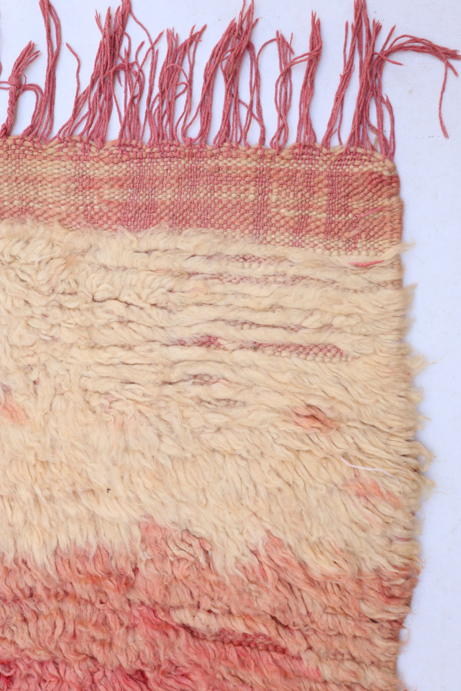 Tapis berbère aux tonalités crème et rouge avec un motif tissé doux et des franges délicates.