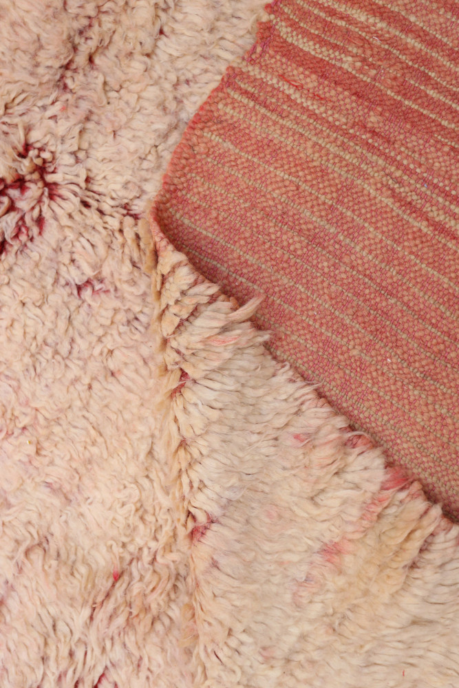 Tapis berbère en laine beige avec motifs en relief, nuances de rose et textures douces et chaleureuses.