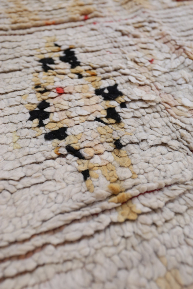 Tapis berbère aux motifs géométriques, principalement beige et jaune, avec des accents noirs et rouges.