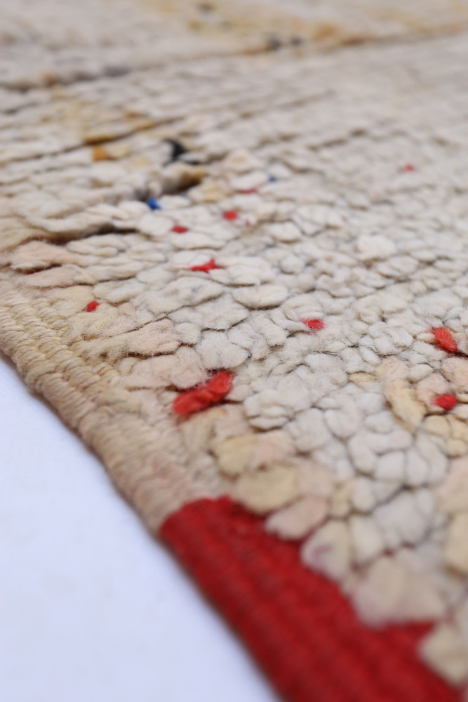 Tapis berbère en laine beige, avec des motifs géométriques et des touches de rouge et bleu vibrants.