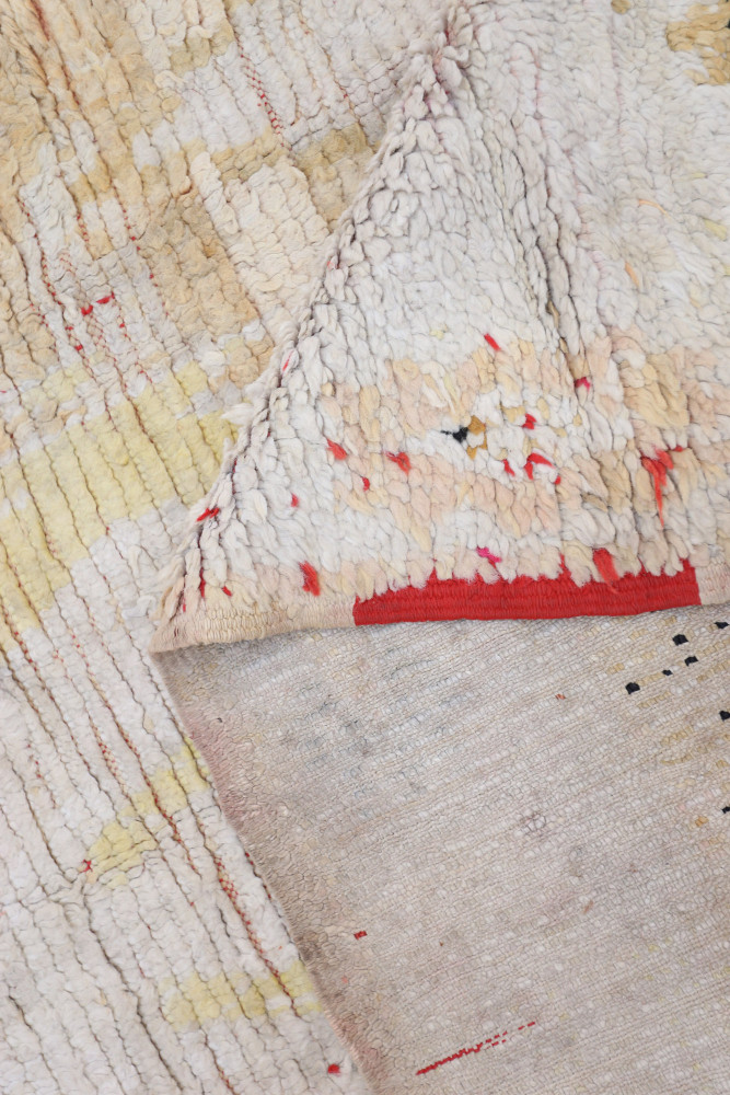 Tapis berbère aux tons crème et rouge, avec des motifs géométriques colorés et un design texturé unique.