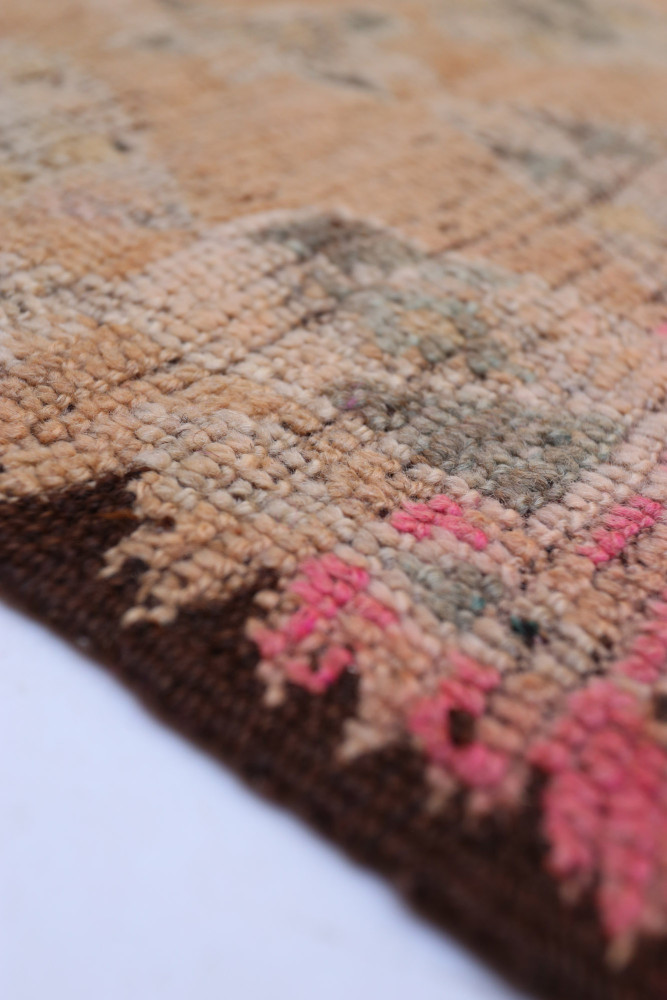 Tapis berbère avec des motifs géométriques en couleurs beige, rose et brun, illustrant un style artisanal unique.