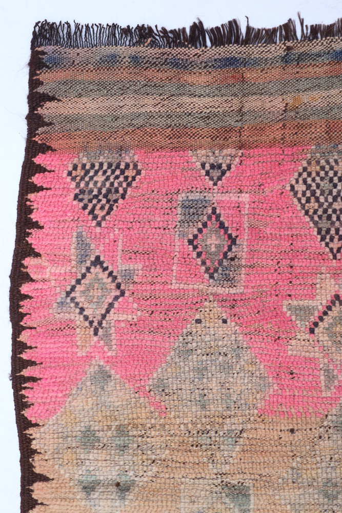 Tapis berbère aux motifs géométriques, dominé par des teintes roses, beiges et noir, ajoutant chaleur et style.