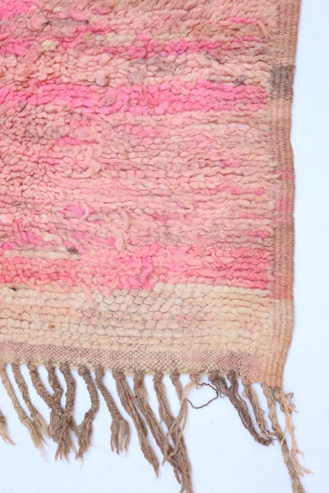 Tapis berbère en laine aux teintes roses et beiges avec des motifs texturés et franges délicates.