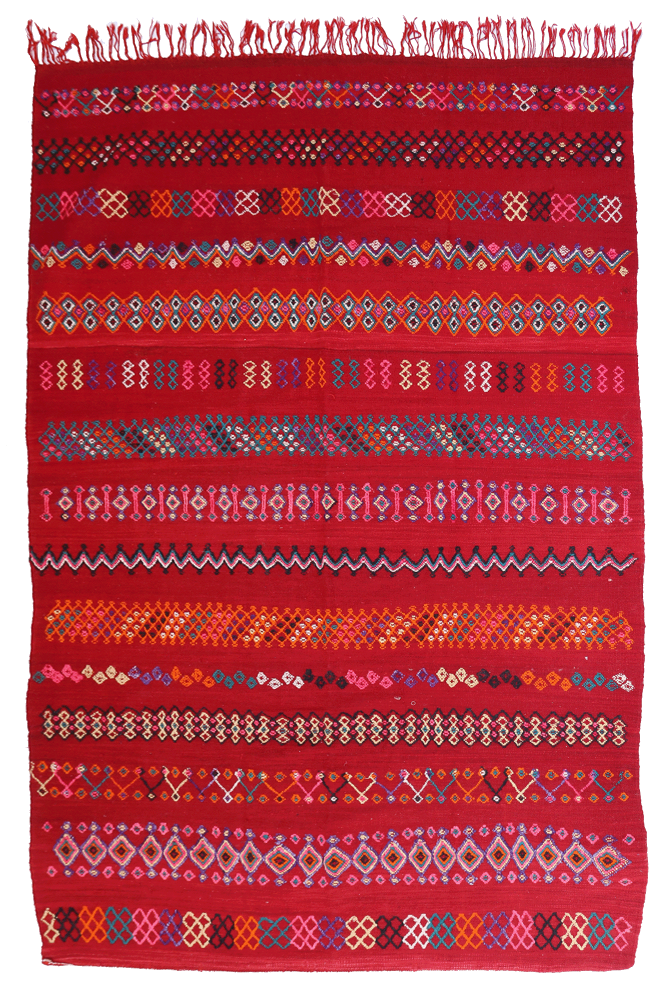 Tapis berbère aux motifs géométriques colorés, dominé par des nuances de rouge et des touches de bleu et d\'orange.