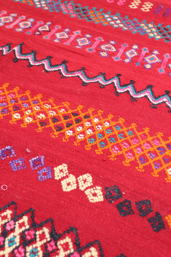 Tapis berbère coloré avec des motifs géométriques en rouge, bleu, jaune et noir, ajoutant une touche artisanale à votre décorati