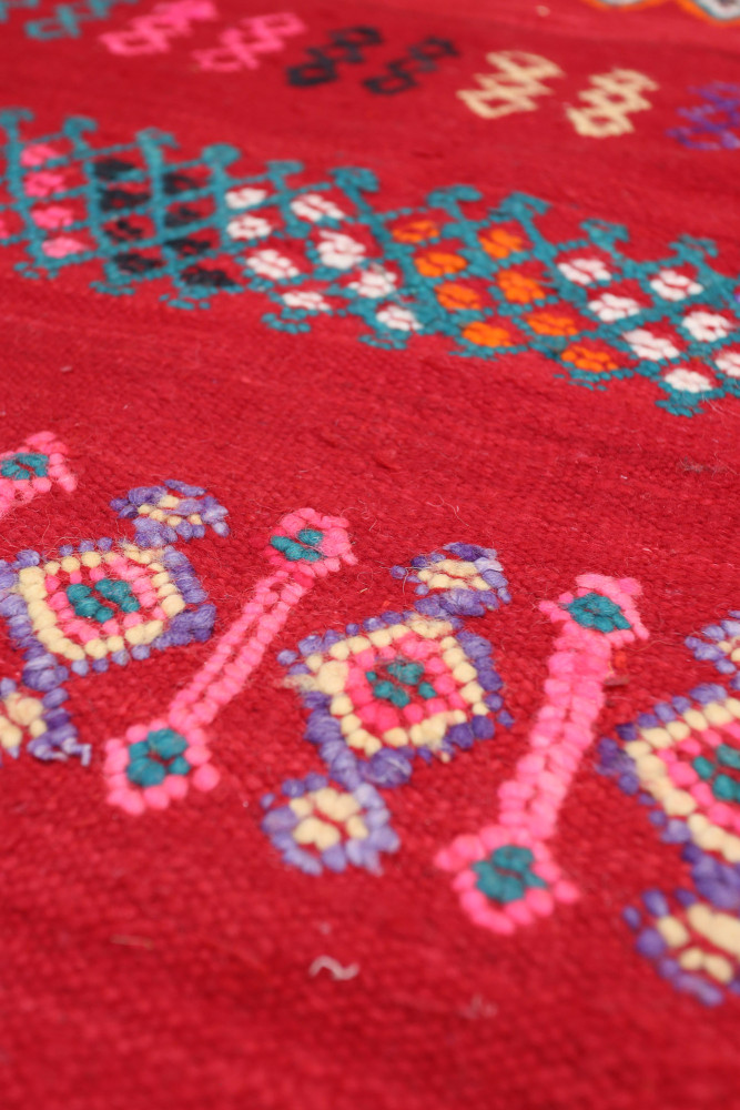 Tapis berbère aux motifs géométriques colorés, dominé par des tons rouges, roses et bleus vibrants.