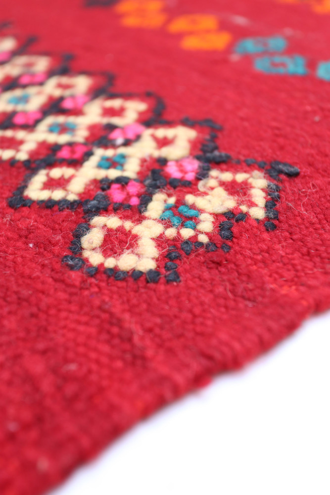 Tapis berbère rouge avec motifs géométriques colorés en noir, rose, orange et bleu, ajoutant une touche artisanale élégante.