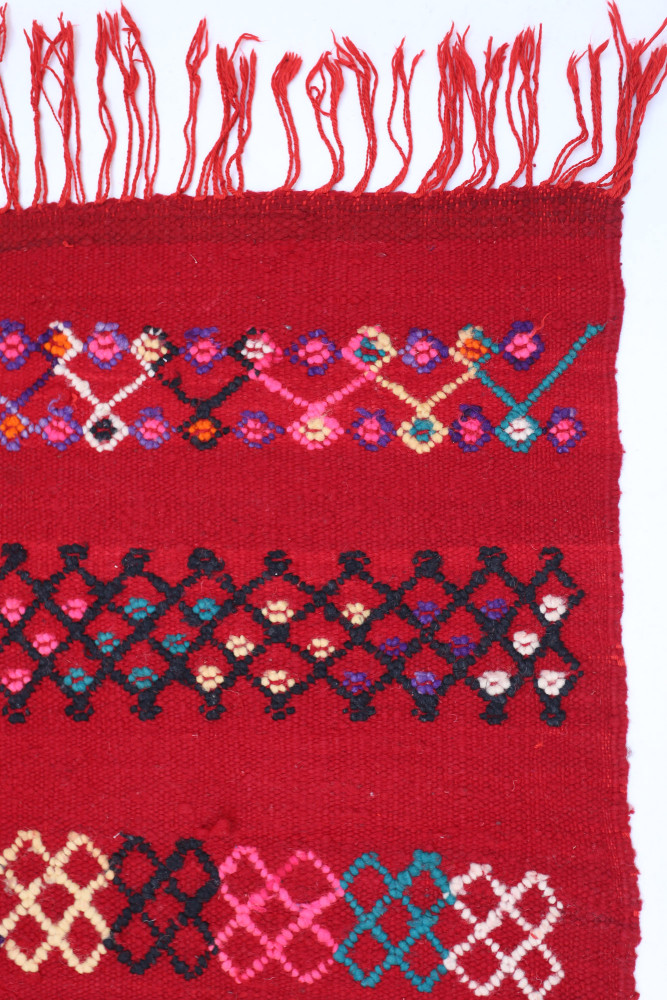 Tapis berbère coloré avec motifs géométriques en rouge, noir, rose et bleu, ajoutant une touche artisanale à tout espace.