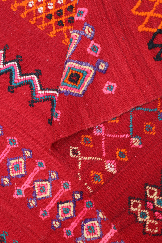 Tapis berbère rouge avec des motifs géométriques en rose, orange et noir qui ajoutent une touche artisanale et colorée.