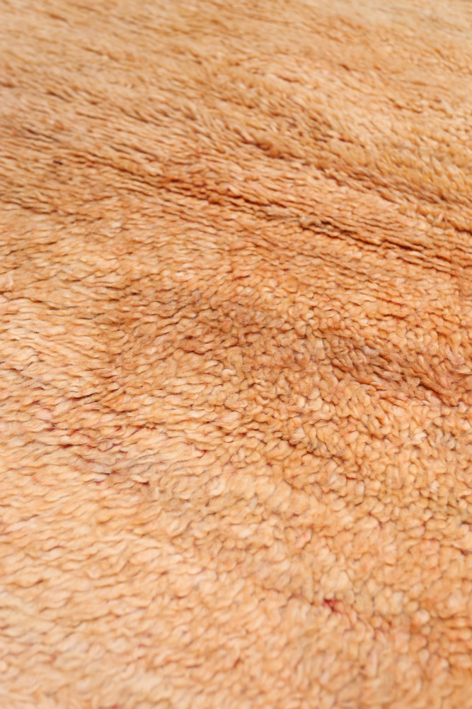Tapis berbère doux en tons orangés avec des textures naturelles et un design minimaliste, idéal pour un intérieur chaleureux.