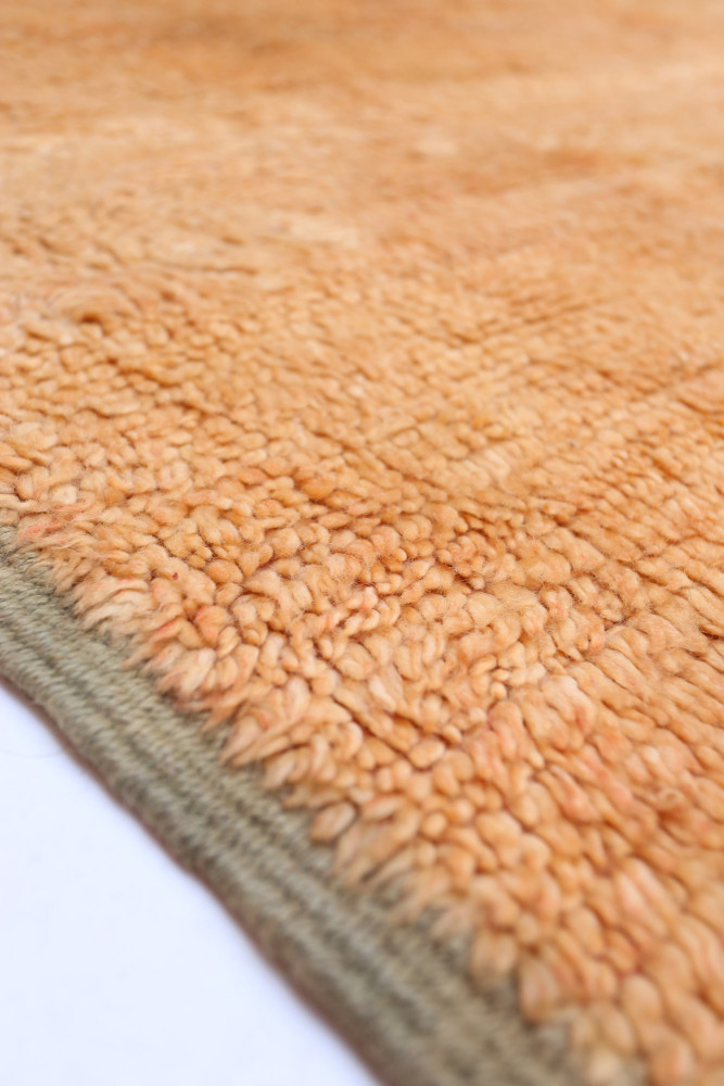 Tapis berbère en laine, couleur orange doux, texture pelucheuse et bordures discrètes, idéal pour un intérieur chaleureux.