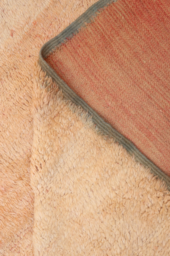 Tapis berbère en teintes de beige et d\'orange, avec des motifs subtils et une texture douce et soyeuse.