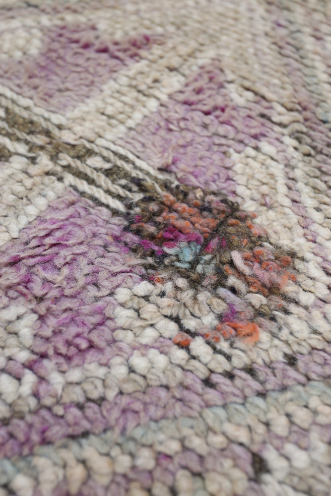 Tapis berbère aux motifs géométriques en teintes de violet, crème et touches d\'orange, offrant un style artisanal unique.