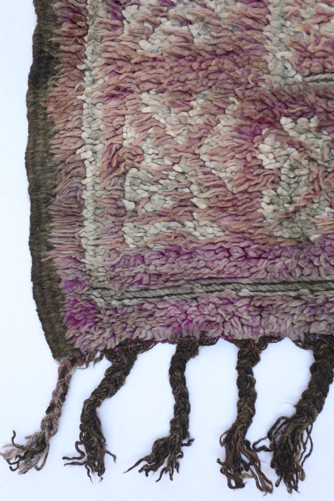 Tapis berbère aux teintes douces de rose et beige, avec des motifs géométriques et franges délicates.