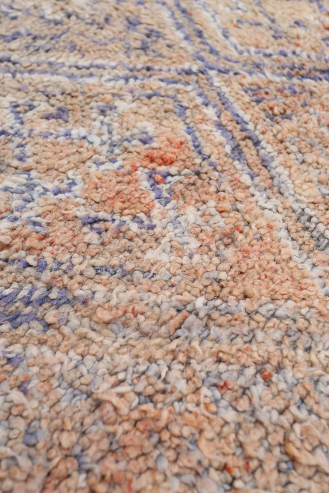 Tapis berbère aux motifs géométriques, aux teintes sable, bleu pastel et touches d\'orange.