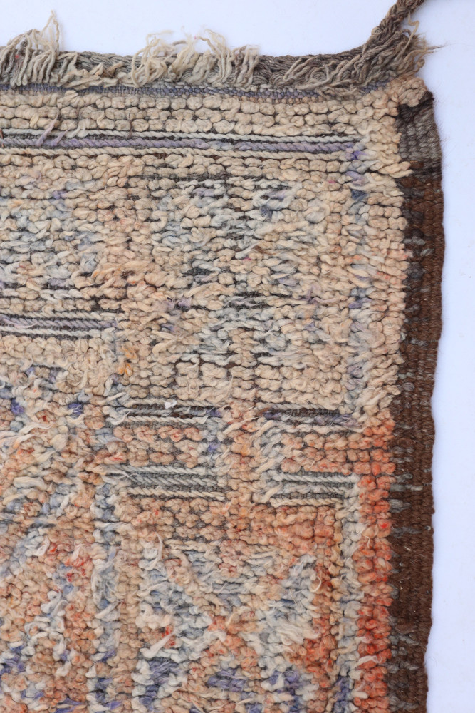 Tapis berbère à motifs géométriques dans des teintes neutres de beige, orange et bleu, ajoutant une touche artisanale.