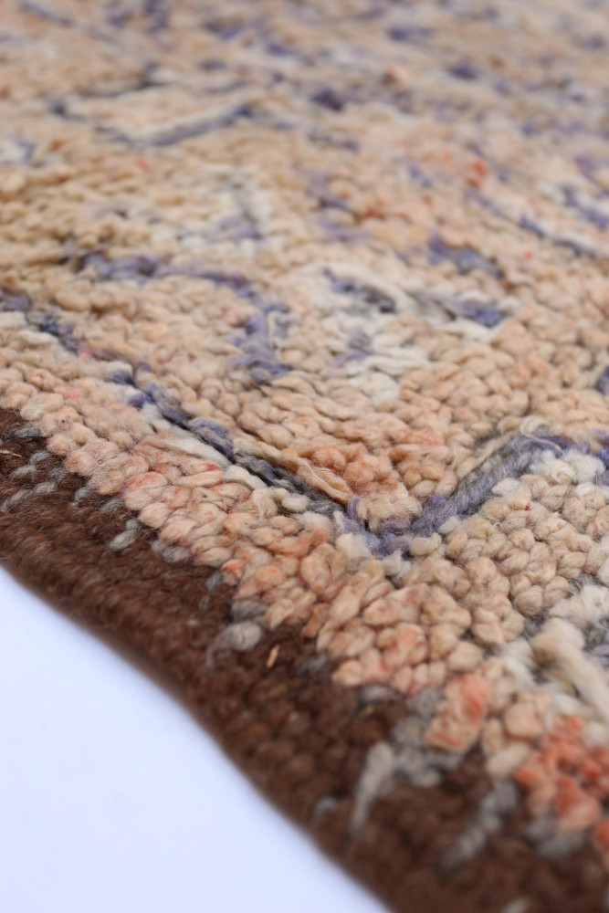 Tapis berbère aux motifs géométriques, dominant les teintes beige et marron avec des touches de violet et d\'orange.